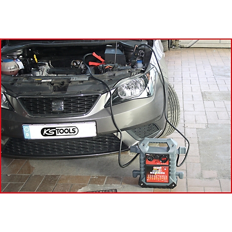 Graues Auto, offene Motorhaube, Starthilfekabel mit Starthilfe-Gerät angeschlossen.